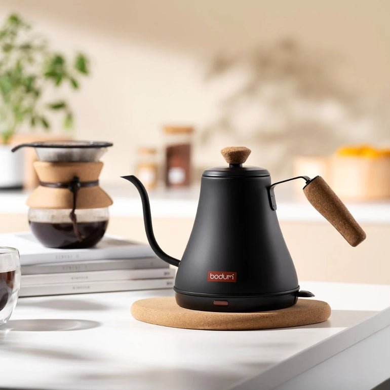 Bodum Melior electric kettle with stainless steel body and black handle, boiling water on a kitchen countertop.