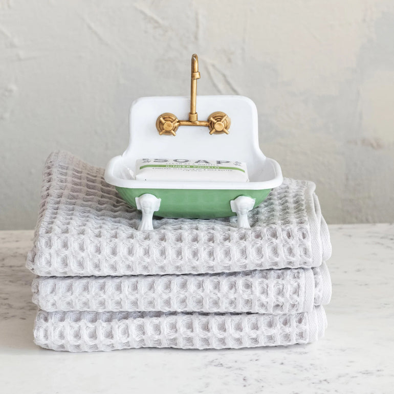 Green and white sink-shaped soap dish with brass faucet and soap bar on gray towels