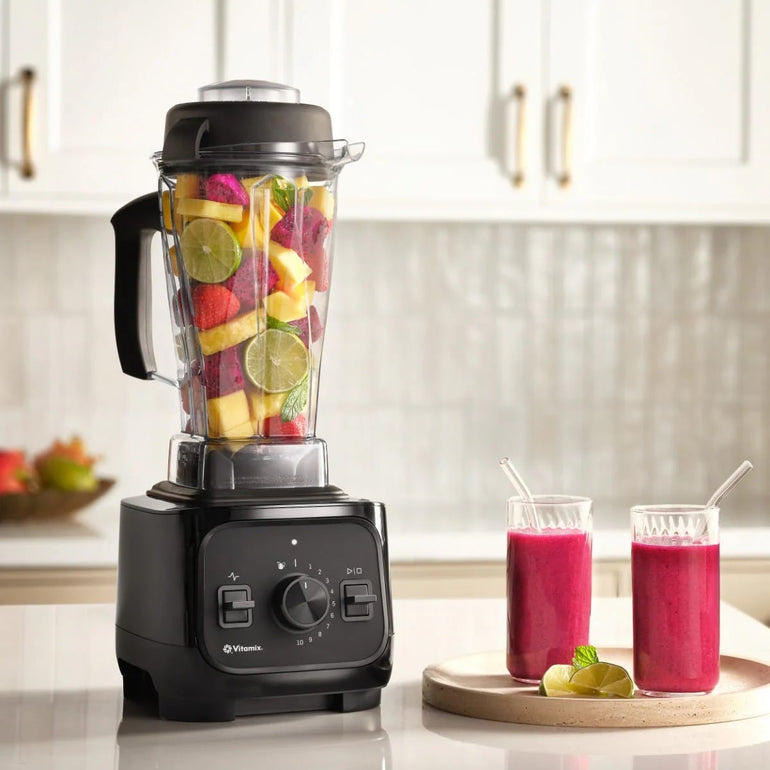 Black Vitamix VX1 blender filled with fruit on a kitchen counter beside two juice glasses