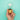 Hand holding a lit filament lightbulb with a gold base against a bright turquoise background