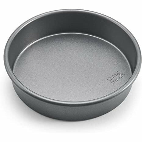 Empty round dark gray non-stick cake pan, angled top-down view on white