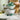 A person is holding a green bowl set, which includes various sized bowls and measuring cups, with a kitchen backdrop.