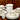 Fish's Eddy Greenband collection — stack of mugs, plates, saucers, and demitasse cups in cream stoneware with green band detail, on a rustic wood surface