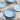 Set of light blue ceramic plates and bowls on a beige surface with white napkins and silverware.