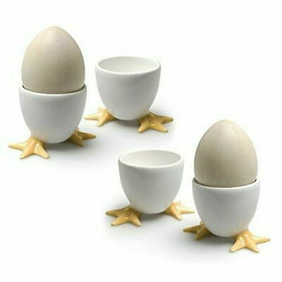 Two white egg cups with yellow chicken feet, one holding a speckled egg, set on white